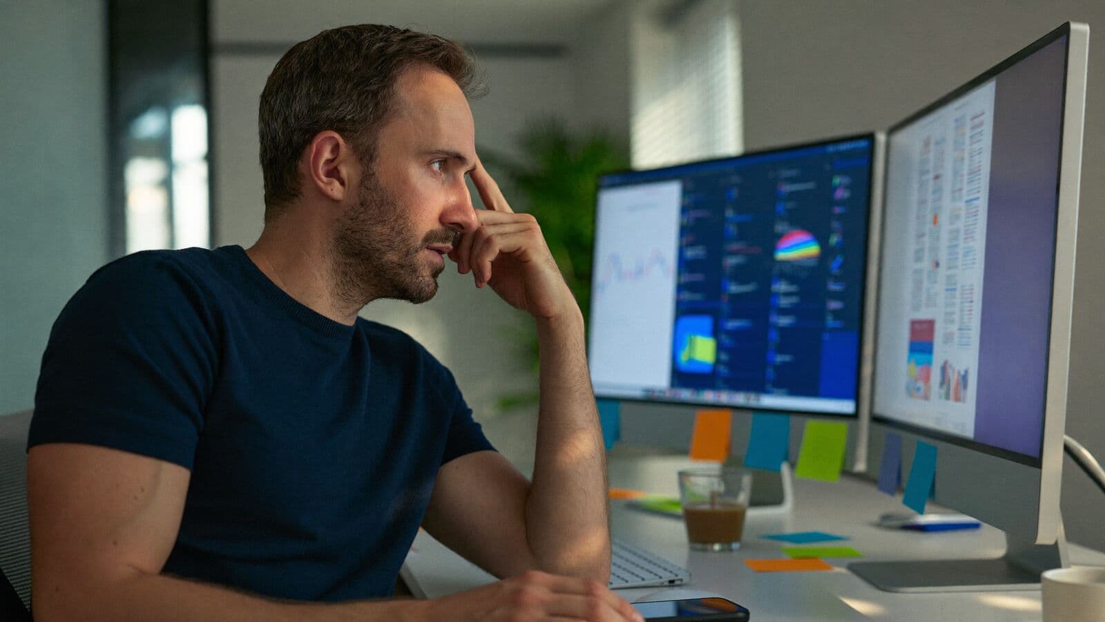 Office manager at a desk with two monitors of different apps and sticky notes