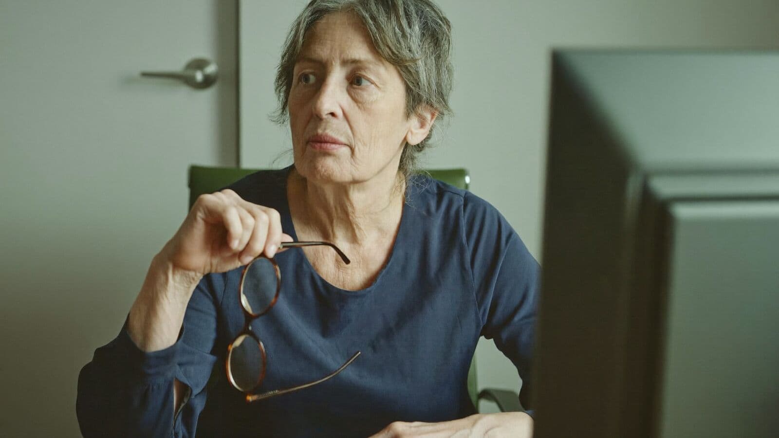Senior manager holding reading glasses while reviewing work at her desk