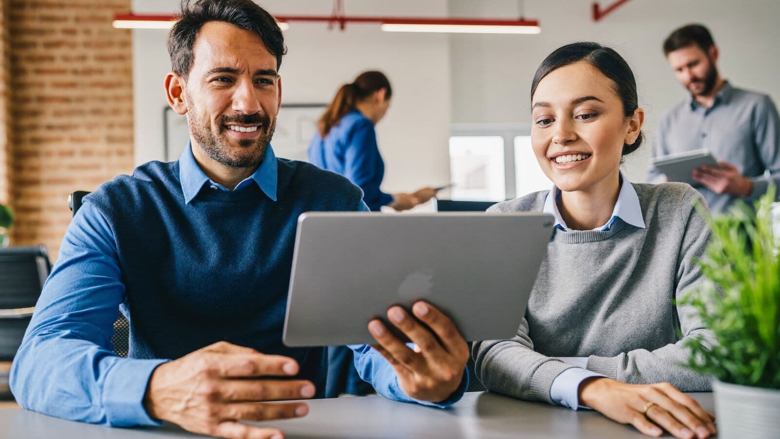 Colleagues reviewing a client handover on a tablet in an open-plan office